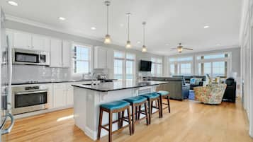 Una cocina moderna con armarios blancos, electrodomésticos de acero inoxidable, una isla grande con taburetes y vistas al exterior.