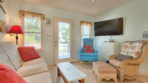 Una sala de estar acogedora con un sofá, un sillón azul, una silla de mimbre, un televisor y una mesita.