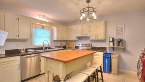Una cocina con armarios blancos, una isla de madera, electrodomésticos de acero inoxidable y un contenedor azul para reciclaje.