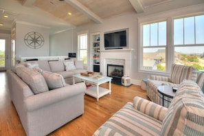 A spacious living room with a fireplace, large windows, and a television. - A Perfect Getaway: Private Pool, Elevator, Walk to Beach (Oak Island)