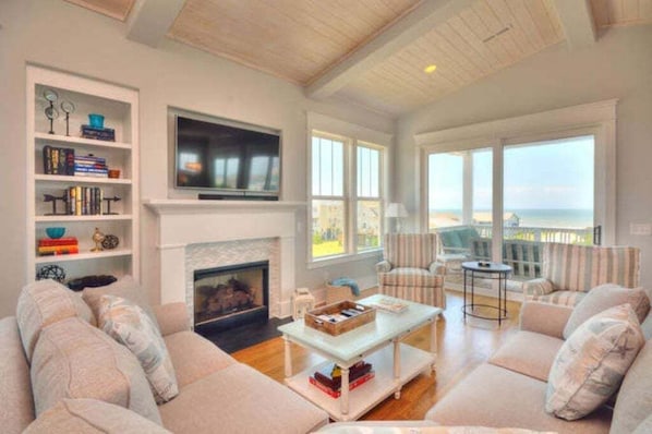 A living room with a fireplace, a television, a sofa, a coffee table, and a view of the ocean. - A Perfect Getaway: Private Pool, Elevator, Walk to Beach (Oak Island)