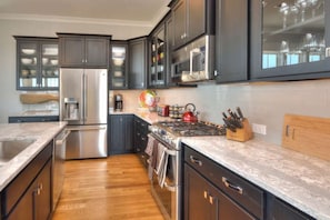 A modern kitchen with dark cabinets, stainless steel appliances, and a wooden countertop. - A Perfect Getaway: Private Pool, Elevator, Walk to Beach (Oak Island)