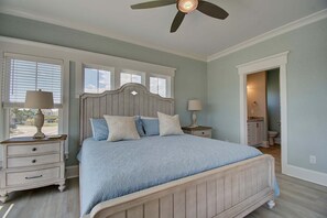 A bedroom with a bed, nightstands, a ceiling fan, and a view of the outside.