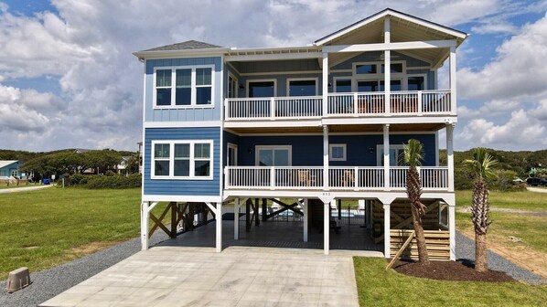 A two-story waterfront house with a balcony on each floor, a covered front porch, and a small garden area.