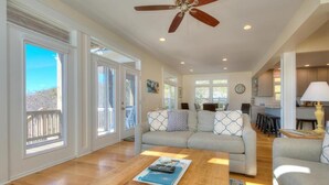 A spacious living room with a wooden coffee table, a grey sofa with patterned cushions, and a ceiling fan. - Oceanview retreat in Oak Island with 4 bedrooms, perfect for family gatherings. (Oak Island)