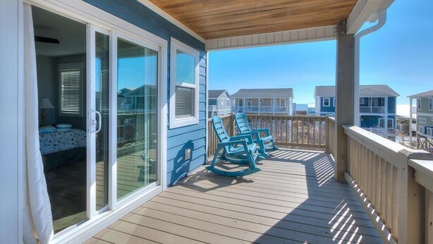 A wooden deck with a glass door leading to a room, and a view of neighboring houses. - Oceanview retreat in Oak Island with 4 bedrooms, perfect for family gatherings. (Oak Island)
