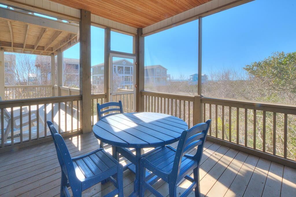 A covered outdoor area with a wooden deck, a round table, and blue chairs.