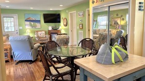 A cozy living room with a dining area, green walls, a flat-screen TV, and a 'Just Beachy' sign.
