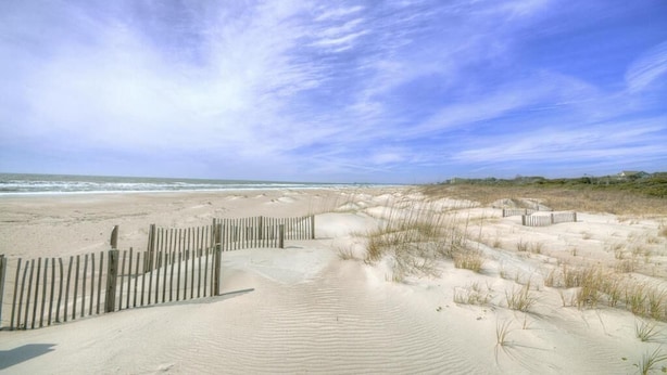 Una platja sorrenca amb una tanca de fusta i dunes.