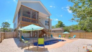 Une maison à deux étages avec un jardin comprenant une piscine, du mobilier d’extérieur et une terrasse en bois.