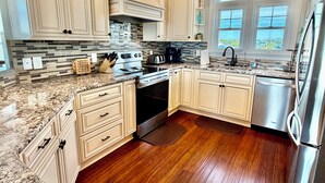 Una cocina con armarios blancos, encimera de granito, refrigerador de acero inoxidable y ventana con vistas.