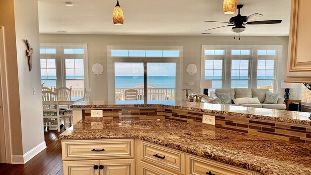 Una cocina con una isla grande, armarios blancos y vista al océano.