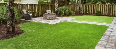 A backyard with a lawn, a wooden fence, a small shed, and a stone fire pit.