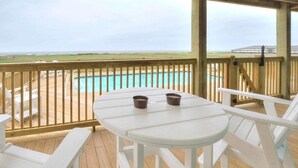 Une terrasse en bois avec une table et des chaises blanches donnant sur une piscine.