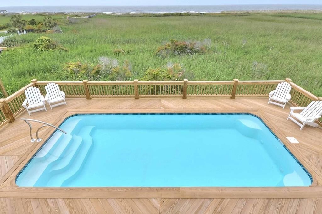 A rectangular pool with a wooden deck and white chairs.