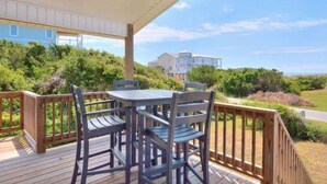 A wooden deck with a table and chairs, surrounded by greenery and overlooking a residential area. - Beach Bungalow in Oak Island—a perfect oceanview retreat for up to 8 guests. (Oak Island)