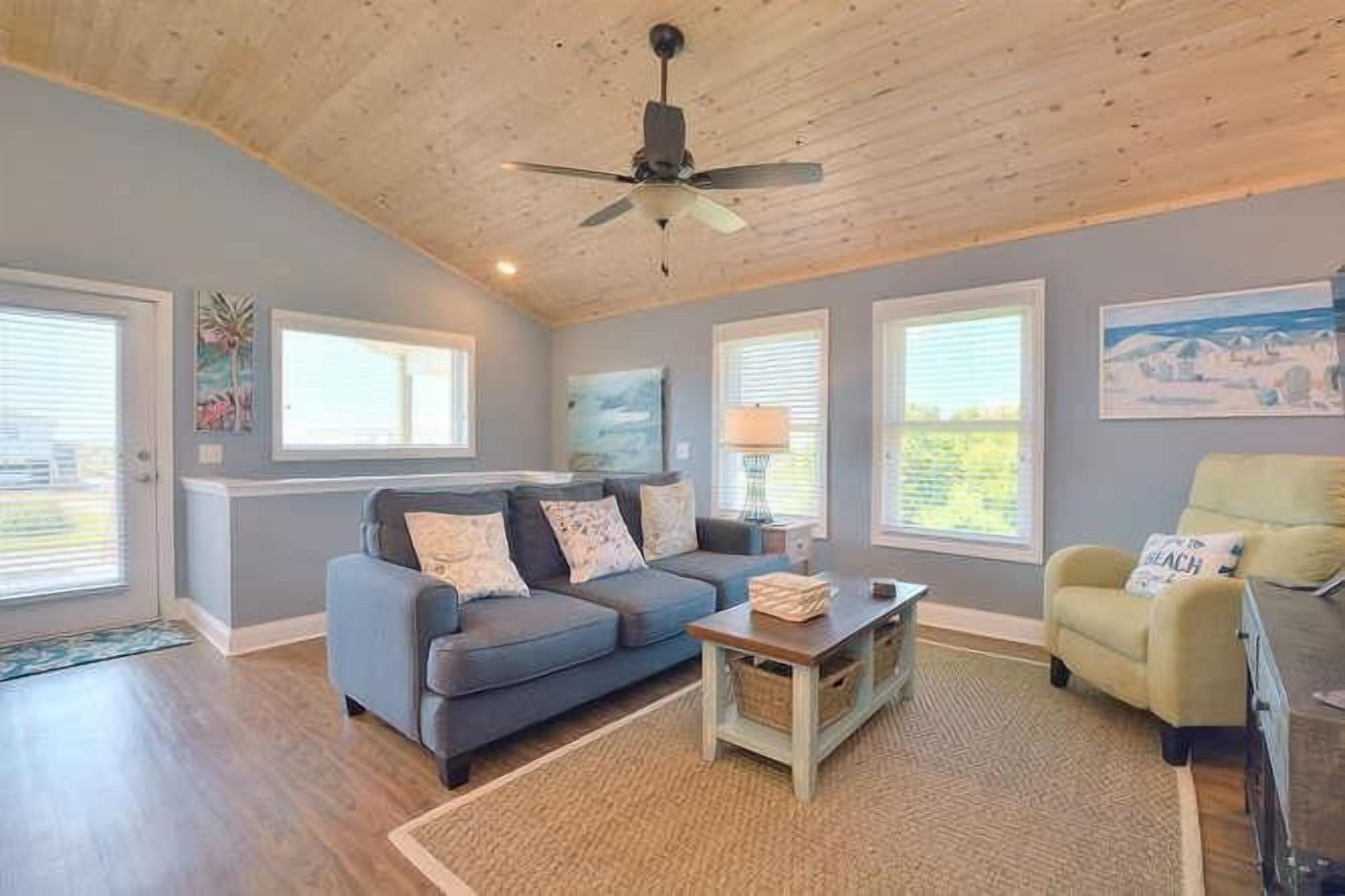 A living room with a blue sofa, a yellow armchair, a wooden coffee table, and a ceiling fan.