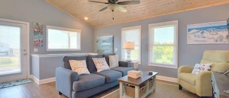 A living room with a blue sofa, a yellow armchair, a wooden coffee table, and a ceiling fan.