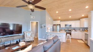 A modern living room with a large flat-screen TV, a grey sofa, a wooden coffee table, and a ceiling fan. - Beach Bungalow in Oak Island—a perfect oceanview retreat for up to 8 guests. (Oak Island)