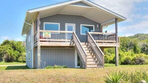 A two-story house with a covered porch and a staircase leading to the upper level. - Beach Bungalow in Oak Island—a perfect oceanview retreat for up to 8 guests. (Oak Island)