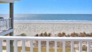 A beach view from a balcony with a wooden railing, sandy beach, and ocean. - Beach Landing: Spacious 7BR/6BA Oceanfront retreat in Oak Island, sleeps 22 with private pool. (Oak Island)