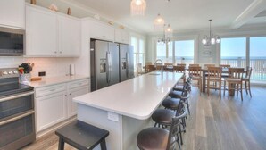 A modern kitchen with white cabinets, stainless steel appliances, and a long island with bar stools. - Beach Landing: Spacious 7BR/6BA Oceanfront retreat in Oak Island, sleeps 22 with private pool. (Oak Island)