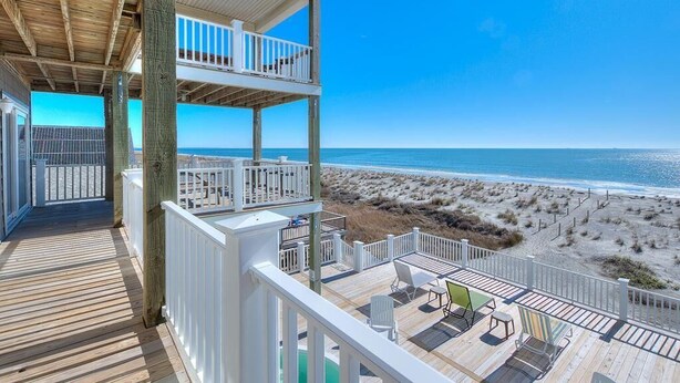A wooden deck with white railings overlooking a beach.