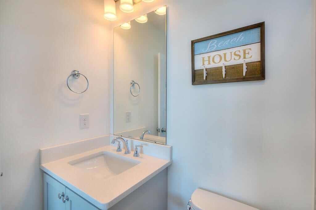 A bathroom with a sink, mirror, and a sign that reads 'Beach HOUSE'.