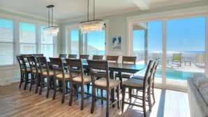 A dining area with a large table and chairs, a chandelier, and a view of the ocean through large windows.