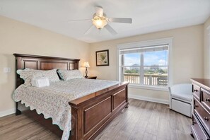 Un dormitorio con cama de madera, ventilador de techo, mesita de noche, cómoda y ventana con vistas.