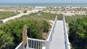 A wooden boardwalk leading to a beach with dunes and sparse vegetation. - Beach Tonic: Oceanfront retreat in Oak Island, this 5BR home accommodates up to 12 guests. (Oak Island)