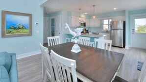 A modern kitchen with white cabinets, stainless steel appliances, and a dining area with a dark wooden table and white chairs. - Beach Tonic: Oceanfront retreat in Oak Island, this 5BR home accommodates up to 12 guests. (Oak Island)