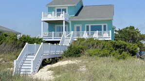 A two-story beachfront house with a balcony and a staircase leading to the entrance. - Beach Tonic: Oceanfront retreat in Oak Island, this 5BR home accommodates up to 12 guests. (Oak Island)