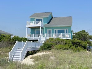 A two-story beachfront house with a balcony and a staircase leading to the entrance.