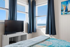 A room with a bed, a TV on a stand, a window with curtains, and a painting on the wall.