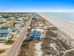 An aerial view of a coastal residential area with houses, a beach, and a road.