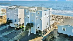 A multi-story beachfront building with a flat roof, multiple balconies, and a sandy beach in the background. - Experience oceanfront luxury at Chasing the Sun, a spacious 7-bedroom retreat in Oak Island. (Oak Island)