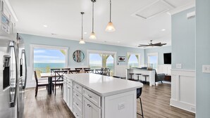 A modern kitchen with a central island, white cabinetry, and a view of the ocean. - Experience oceanfront luxury at Chasing the Sun, a spacious 7-bedroom retreat in Oak Island. (Oak Island)