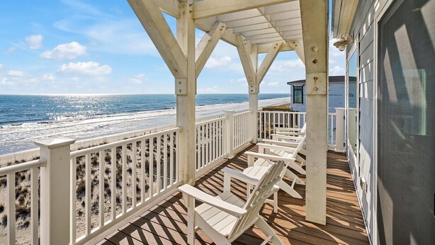 A wooden deck with white railings overlooking a beach. - Experience oceanfront luxury at Chasing the Sun, a spacious 7-bedroom retreat in Oak Island. (Oak Island)