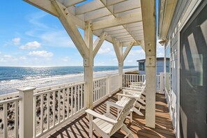 A wooden deck with white railings overlooking a beach.