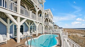 A poolside area with a wooden deck, white railings, and lounge chairs. - Experience oceanfront luxury at Chasing the Sun, a spacious 7-bedroom retreat in Oak Island. (Oak Island)
