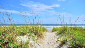 A beach path leading to the ocean with tall grass on either side. - Comin in Hot: Spacious 4-bedroom oceanview home in Oak Island with private pool! (Oak Island)