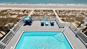 A swimming pool with lounge chairs and a deck overlooking a beach. - Experience oceanfront luxury at Cordoba, a spacious 7-bedroom retreat in Oak Island! (Oak Island)