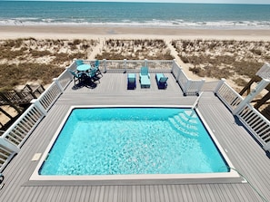 A swimming pool with lounge chairs and a deck overlooking a beach.