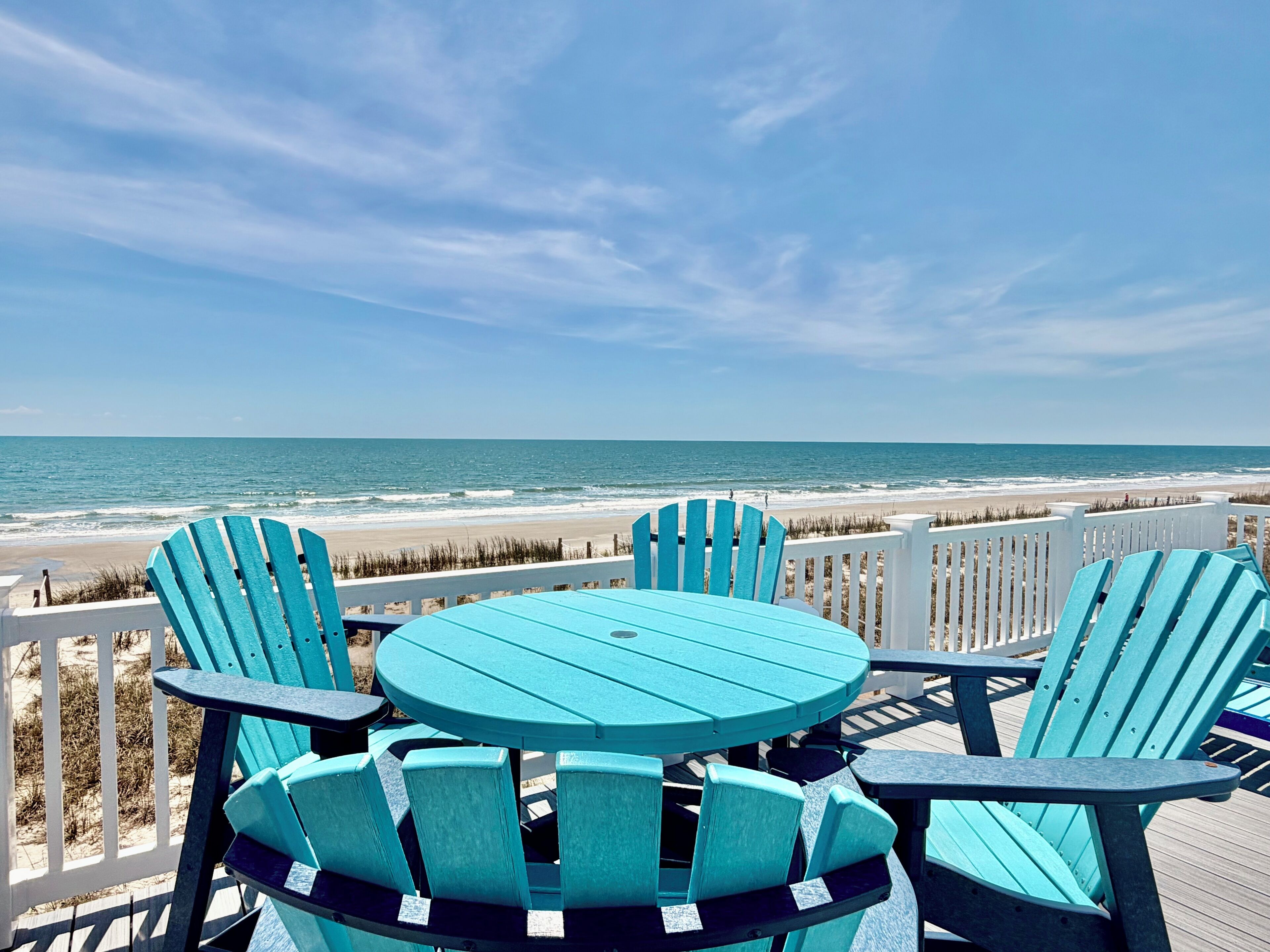 A deck with chairs and a table overlooking a beach.