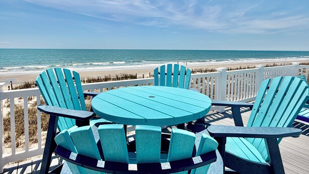 A deck with chairs and a table overlooking a beach. - Experience oceanfront luxury at Cordoba, a spacious 7-bedroom retreat in Oak Island! (Oak Island)