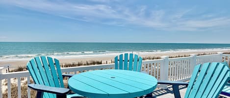 A deck with chairs and a table overlooking a beach.
