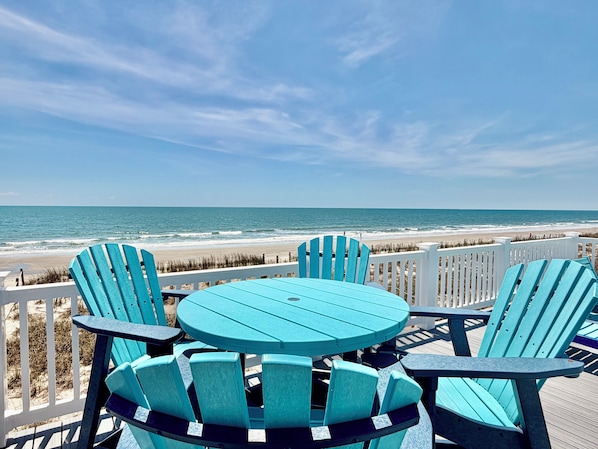 A deck with chairs and a table overlooking a beach.