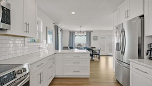 Une cuisine moderne avec des meubles blancs, des appareils en acier inoxydable et un îlot central.