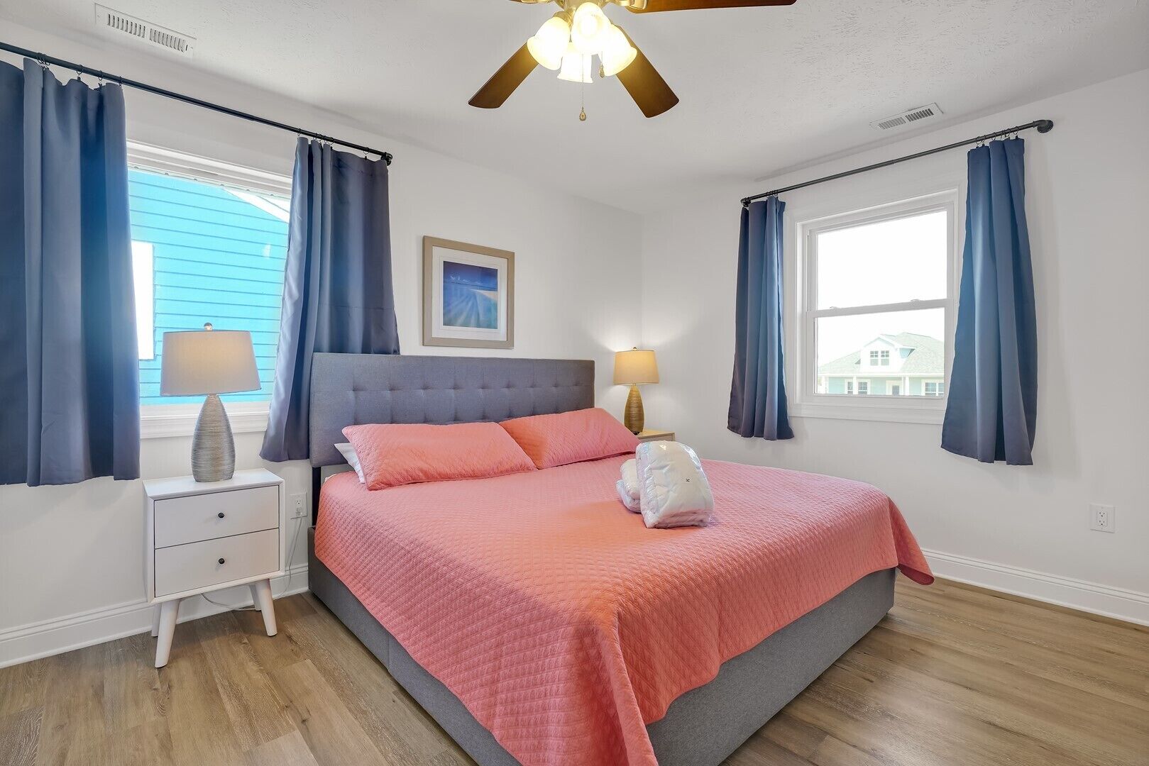 A bedroom with a bed, two bedside tables, a ceiling fan, and a window with curtains.